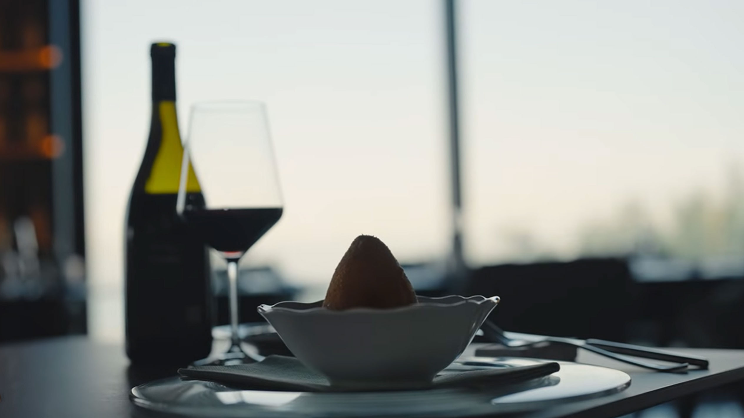 Boca crnog vina i čaša pored jednog arancina u zdjeli na stolu.