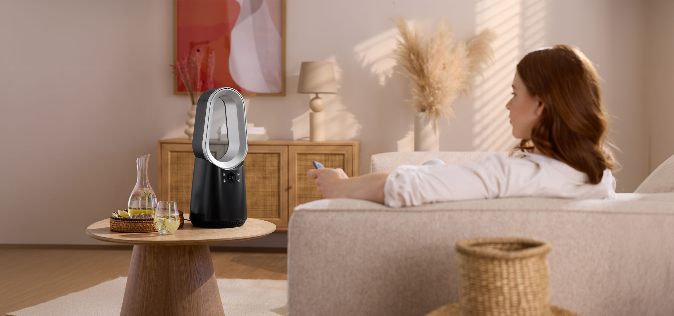 Žena na kauču s daljinskim upravljačem, moderni ventilator i pića na stolu.