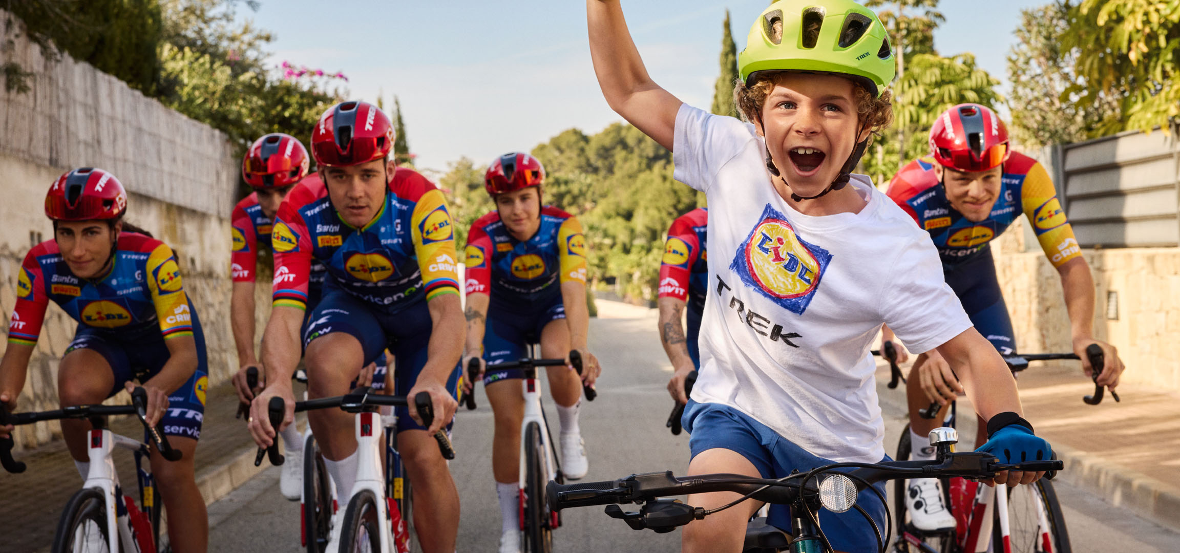 Dijete s kacigom i majicom s Lidl logom, okruženo biciklistima.