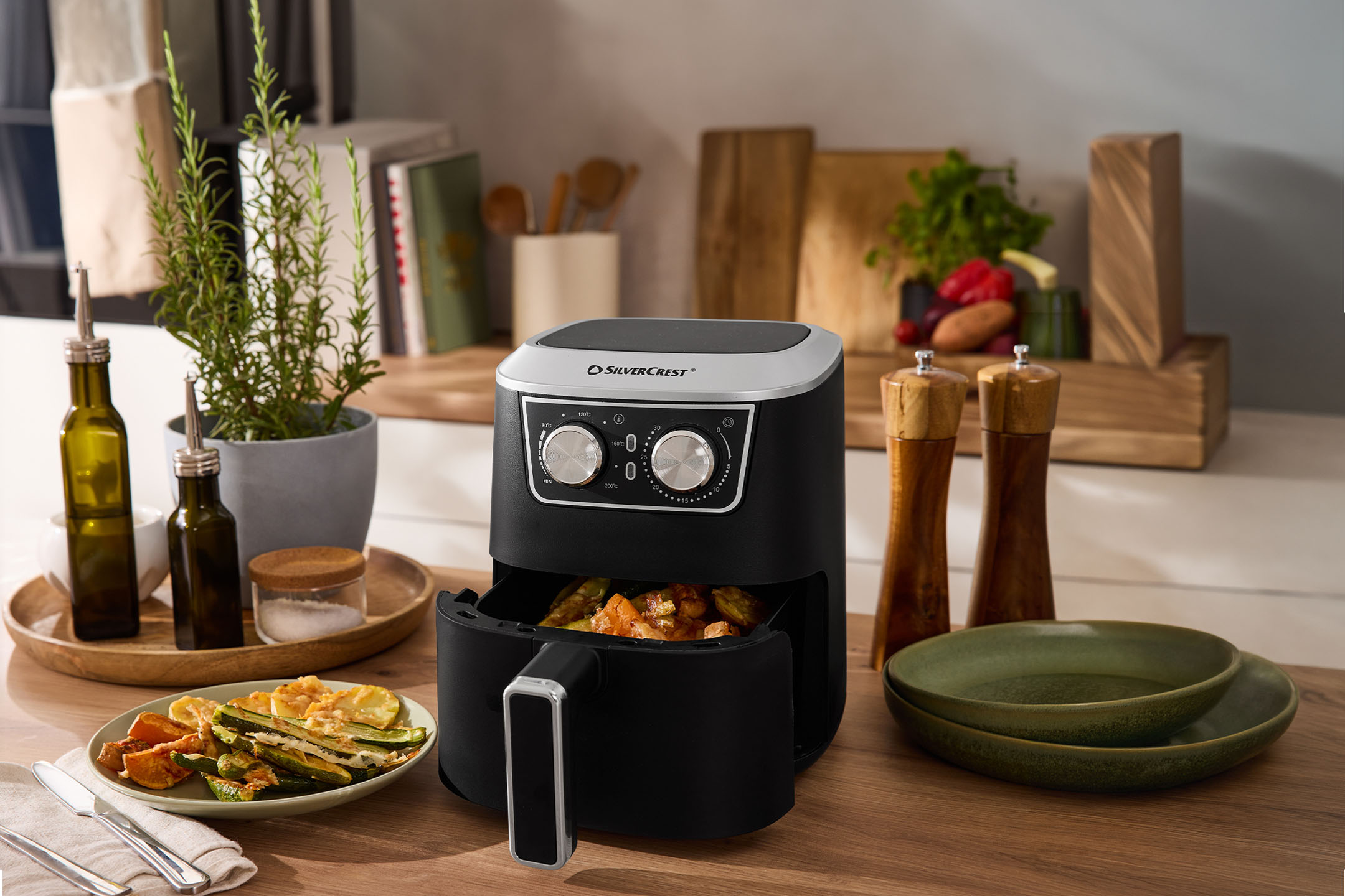 Friteza na vrući zrak s pečenim povrćem, maslinovim uljem, soli i paprom na kuhinjskom pultu.