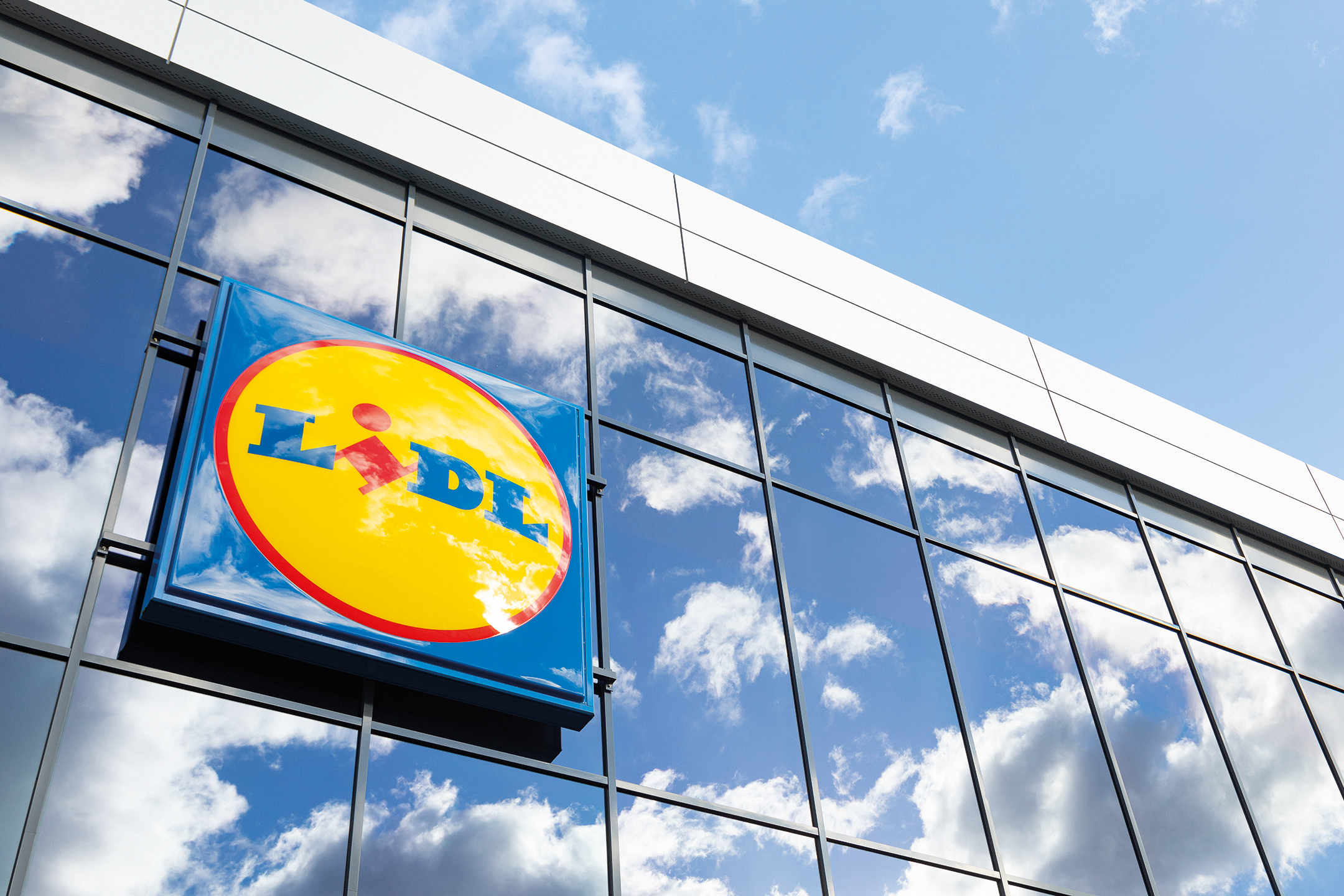 Lidl natpis na staklenoj fasadi zgrade, s odrazom neba i oblaka.
