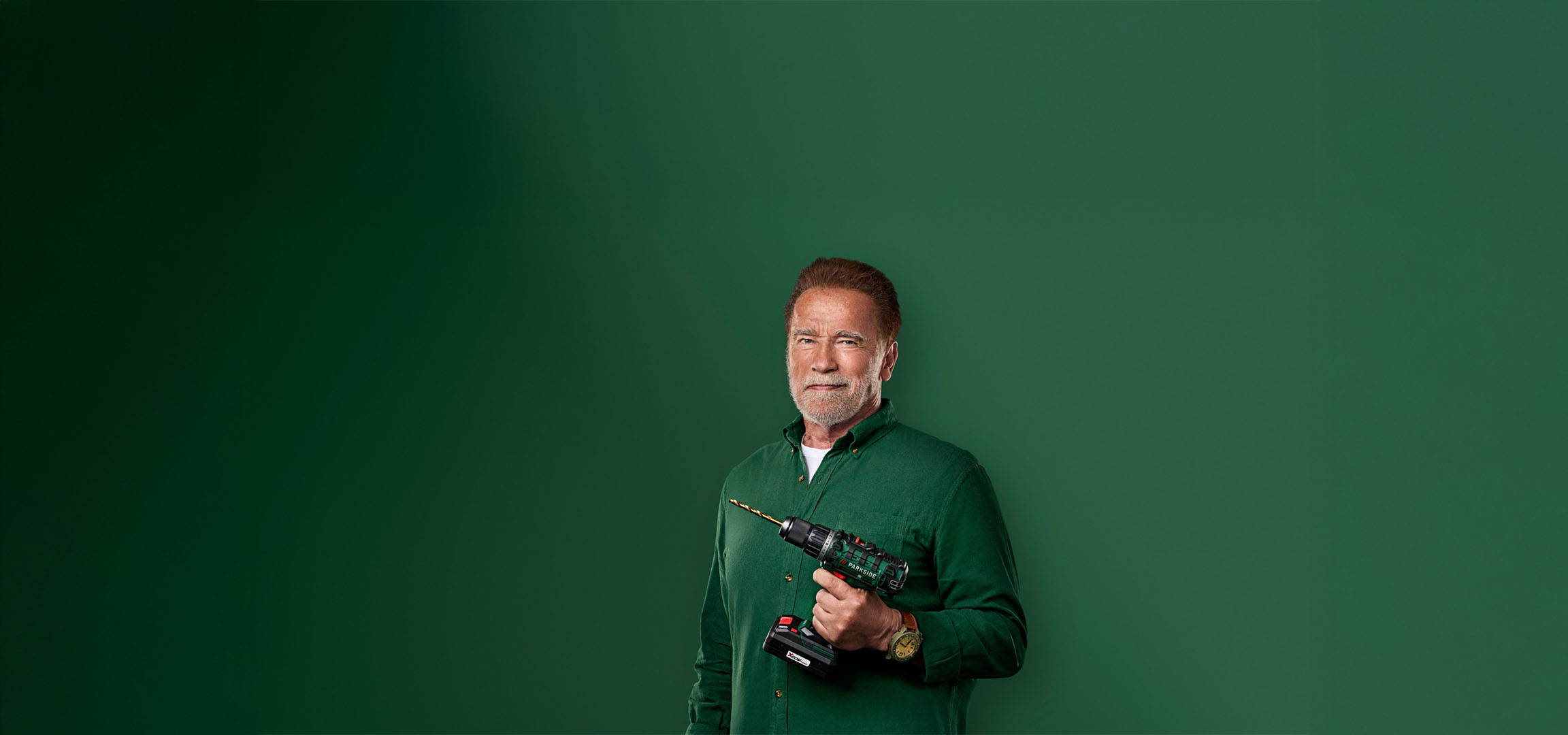 Arnold Schwarzenegger drži bušilicu Parkside na zelenoj pozadini.
