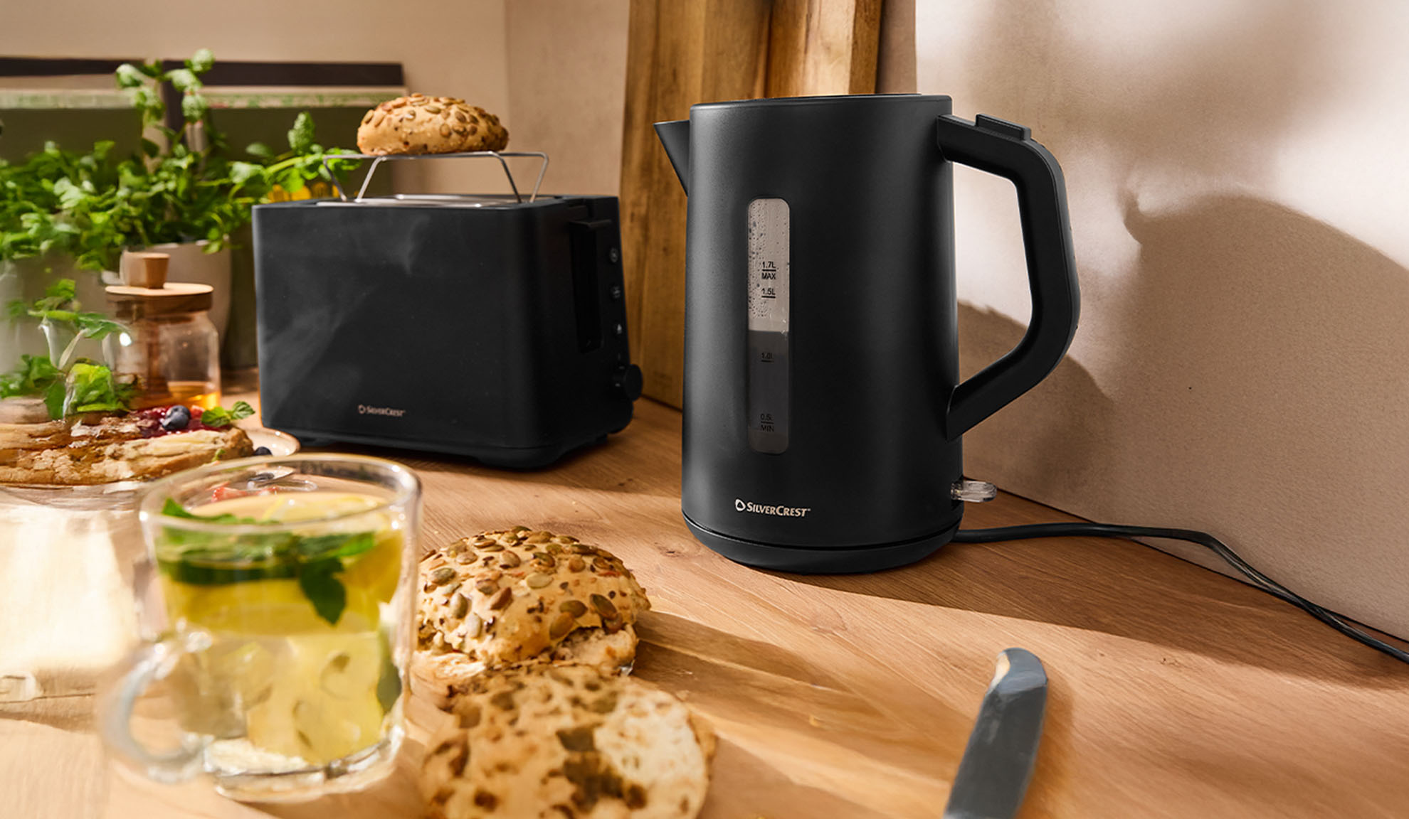 Crno SilverCrest kuhalo za vodu i toster na drvenom stolu s doručkom.