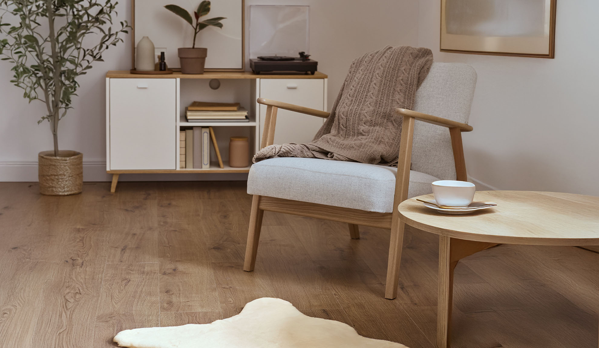 Udobna fotelja s dekom, drveni stolić za kavu i ormarić za pohranu u svijetloj dnevnoj sobi.