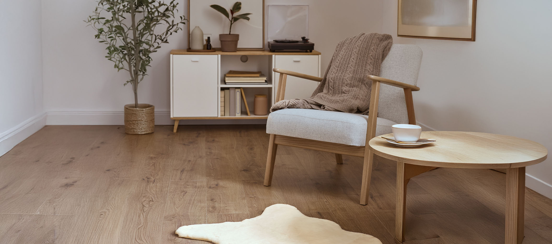 Siva fotelja od tkanine s pletenom dekom, drveni stolić za kavu i moderni ormarić.