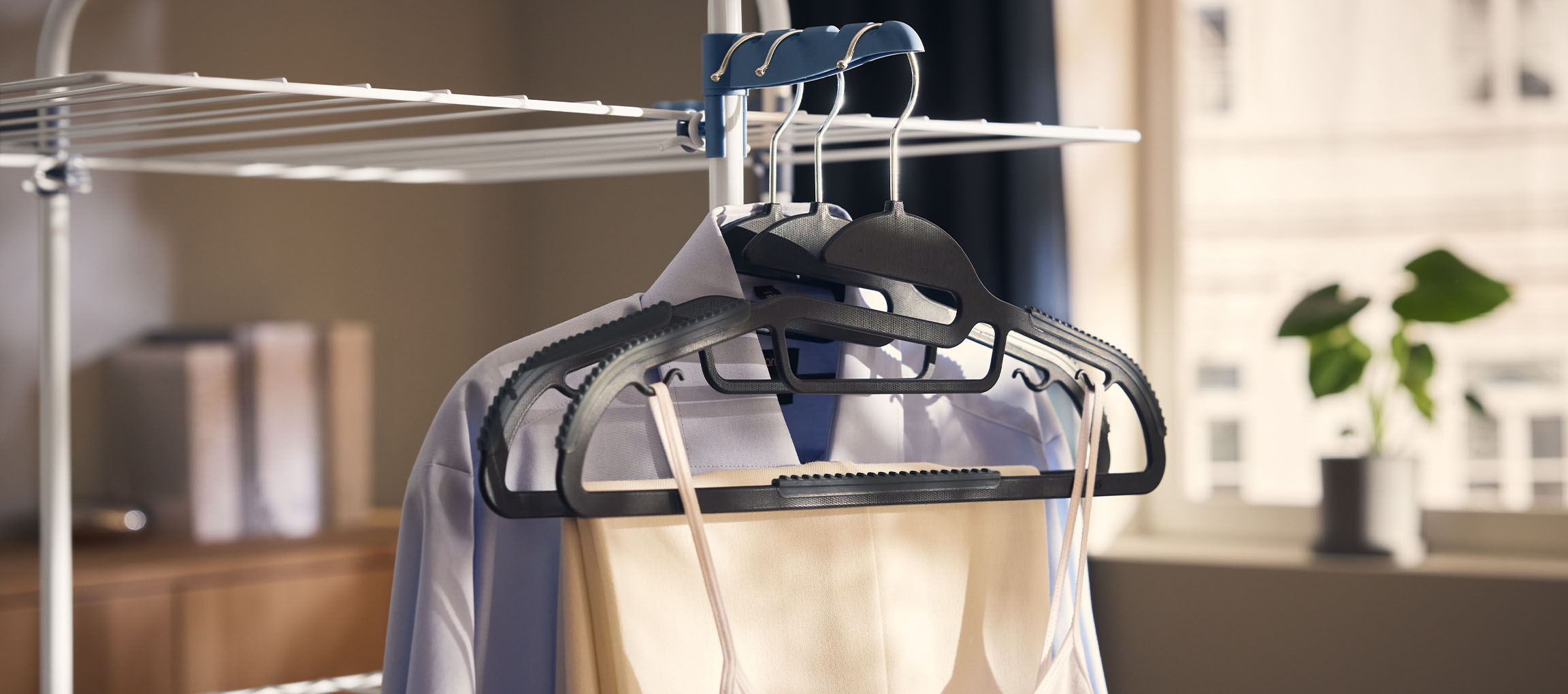 Odjeća na vješalicama na sušilu za rublje, s biljkom u pozadini.