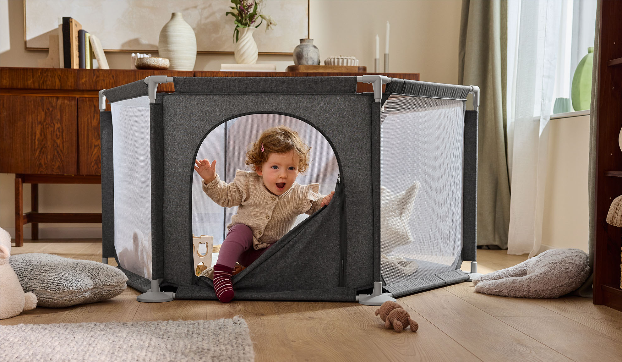 Sretna beba izlazi iz sivog vrtića u ugodnoj dnevnoj sobi.