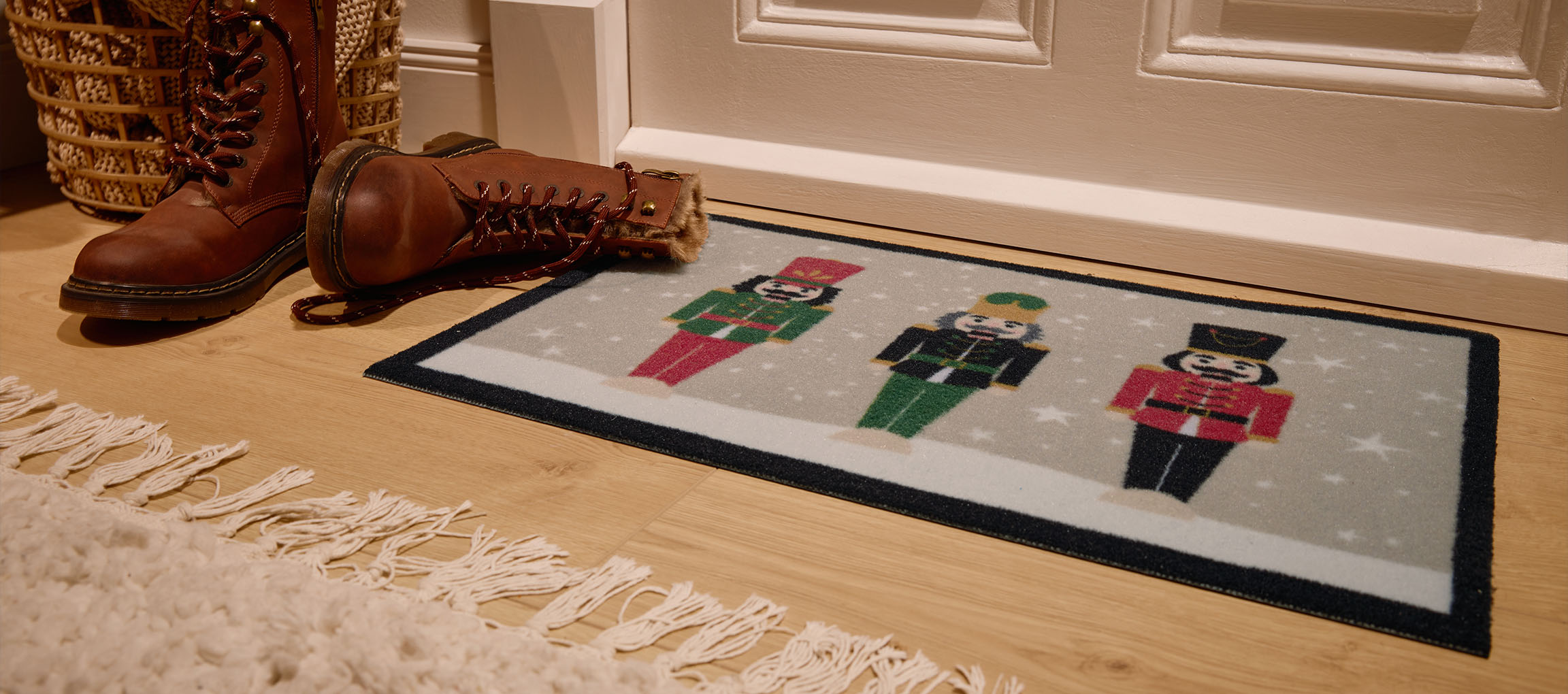 Božićni otirač s orašarima, smeđe čizme i pletena košara na ulazu.