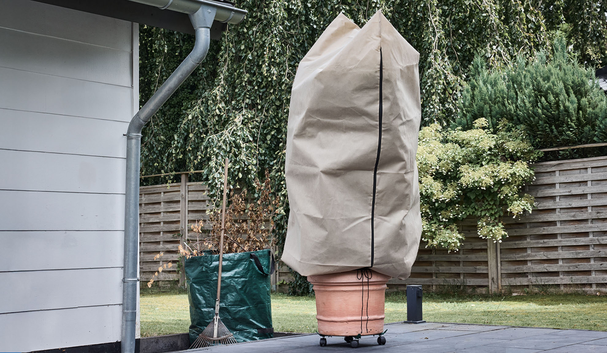 Prekrivač za biljke u tegli na terasi s olukom i grabljama.