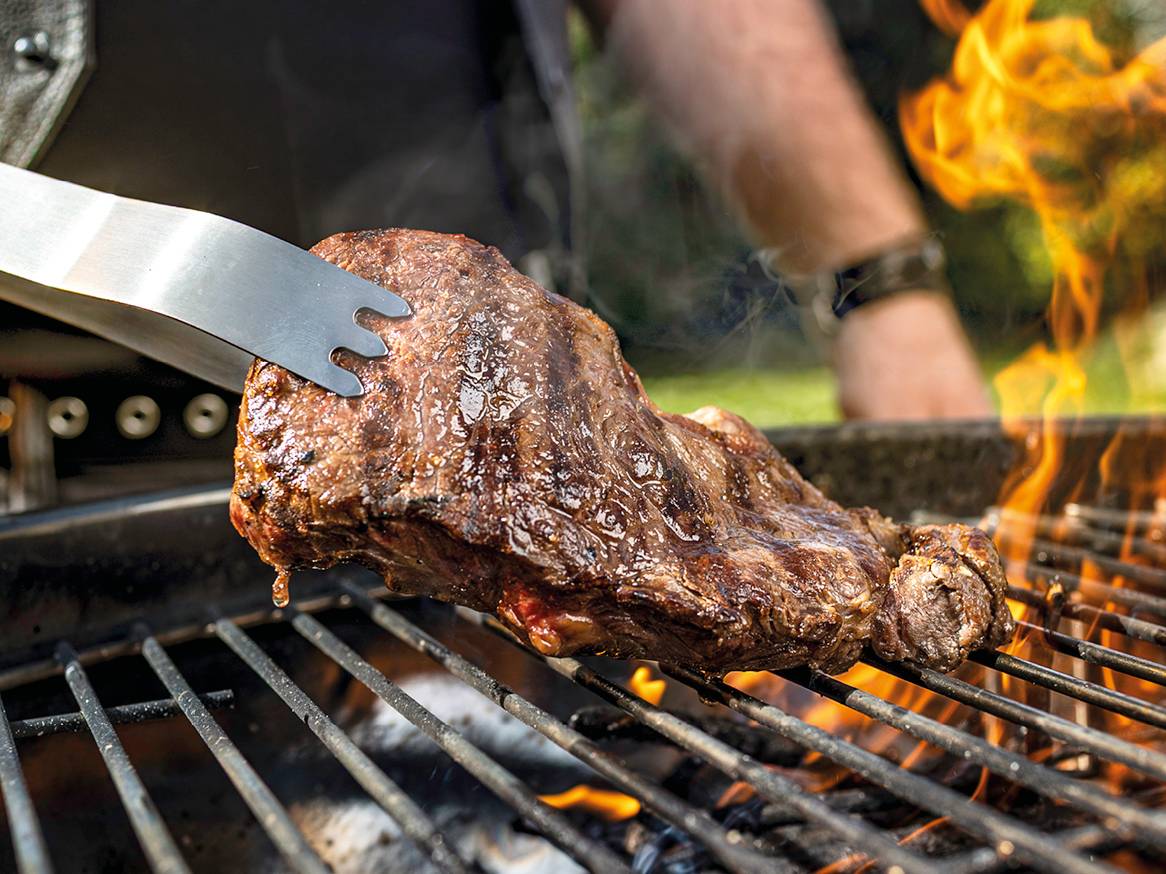 Odrezak na roštilju s hvataljkama i plamenom.