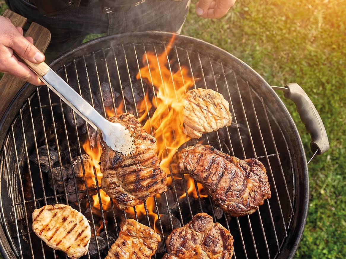 Meso na roštilju s plamenom i rukom koja okreće odrezak hvataljkama.