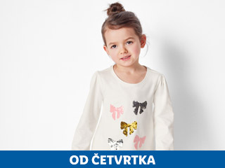Djevojčica u bijeloj majici s dugim rukavima i šljokičastim mašnama.