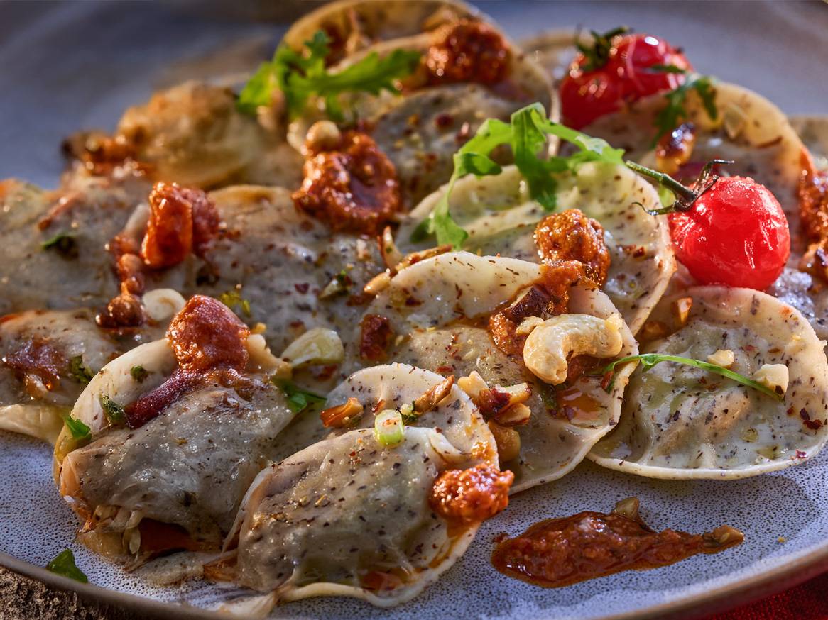 Ravioli s umakom od rajčice, indijskim oraščićima i cherry rajčicama na tanjuru.