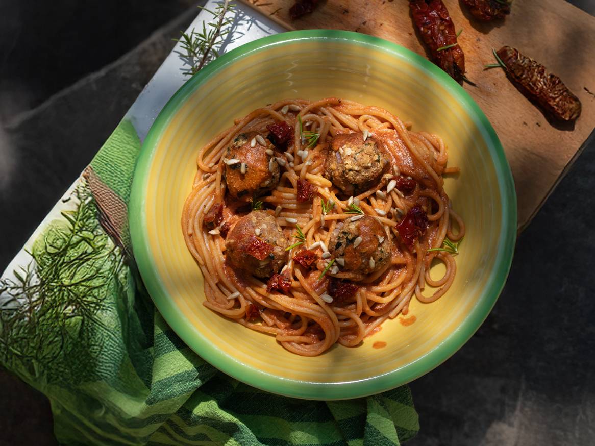 Špageti s umakom od rajčice, okruglicama i sjemenkama suncokreta u žutoj zdjeli.