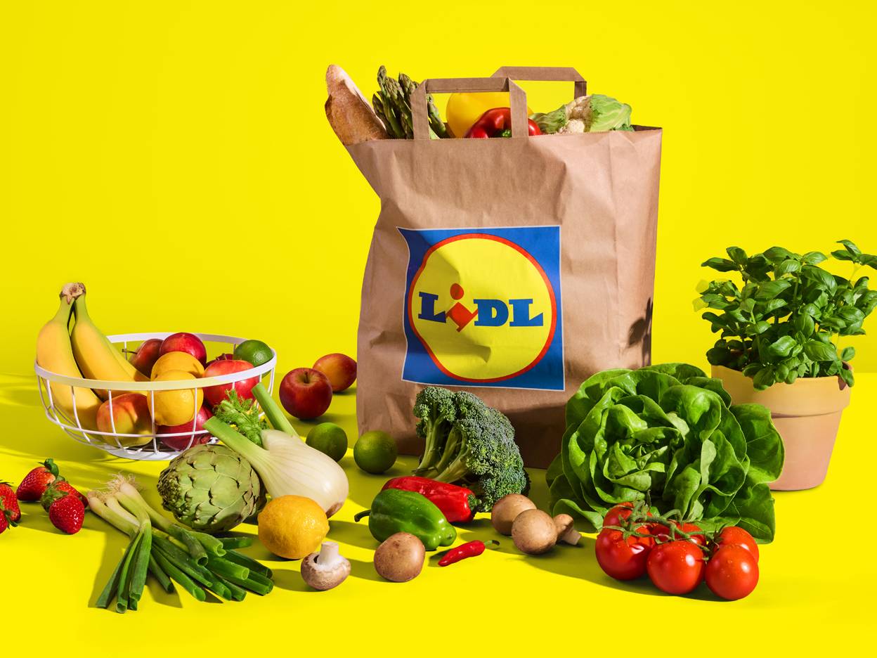 Papirnata vrećica s logotipom Lidla i raznovrsnim svježim voćem i povrćem.