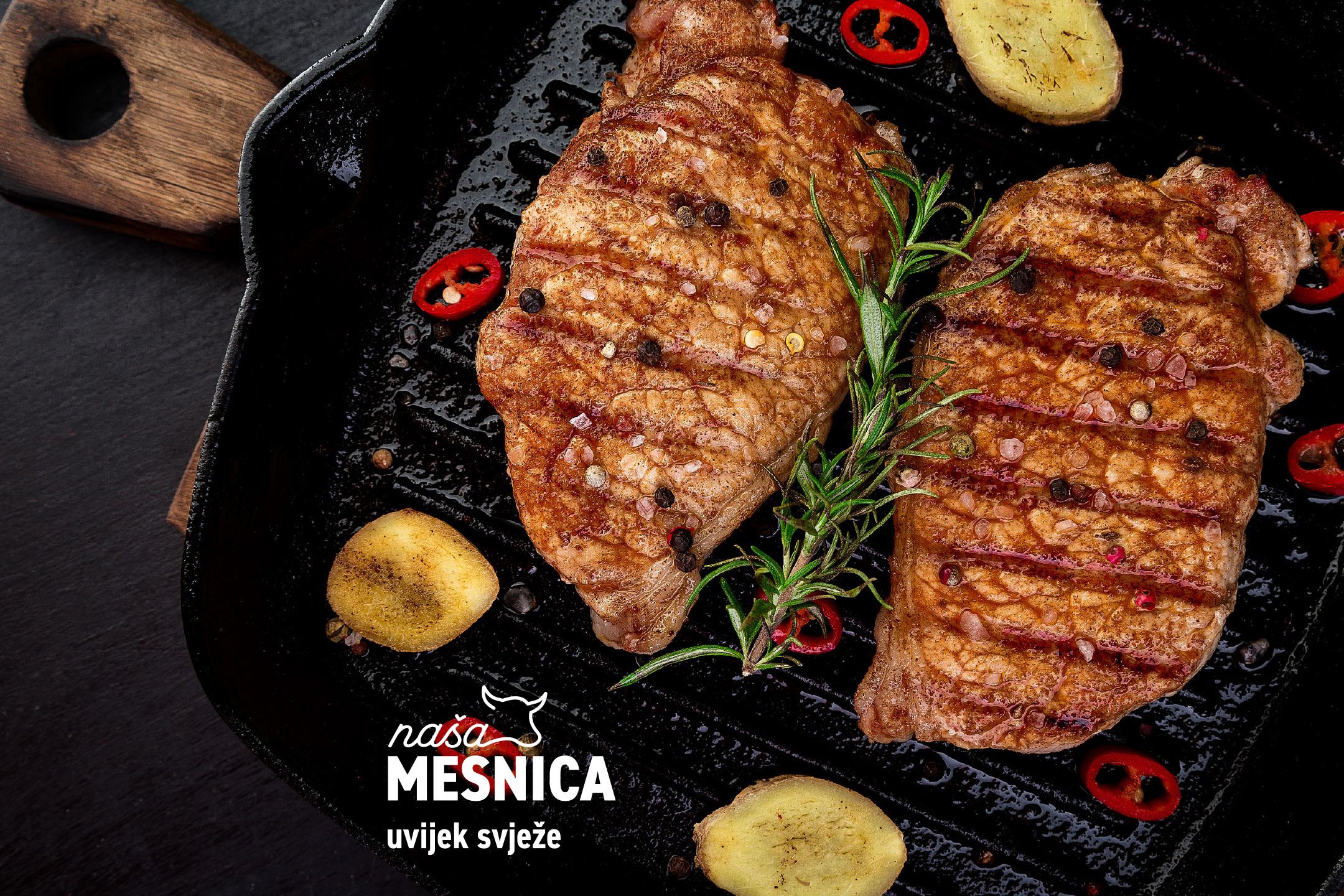 Dva pečena odreska s ružmarinom, paprom i čilijem u tavi, s logotipom 'Naša Mesnica'.