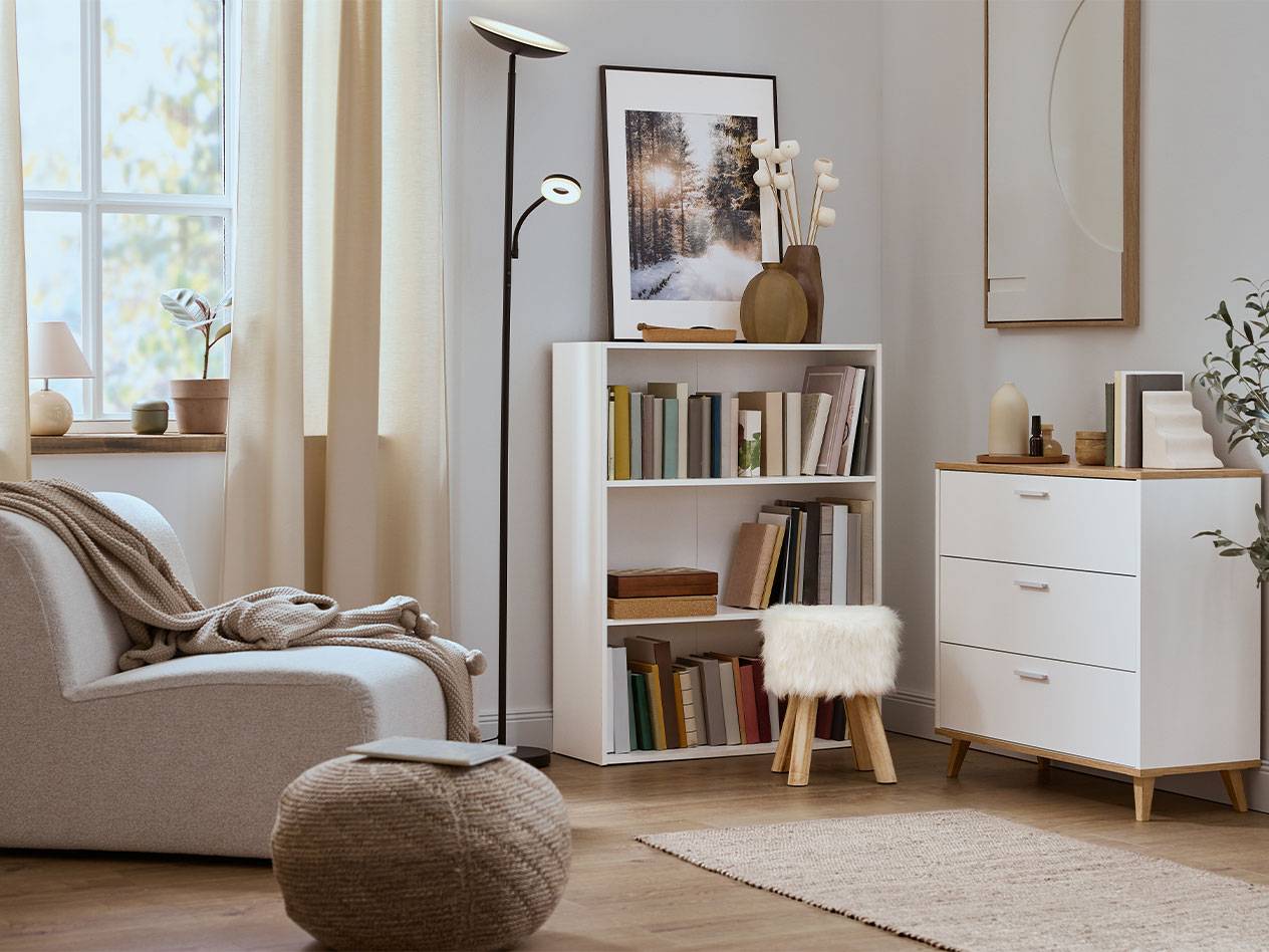 Ugodan dnevni boravak s foteljom, policom za knjige i komodom u neutralnim bojama.