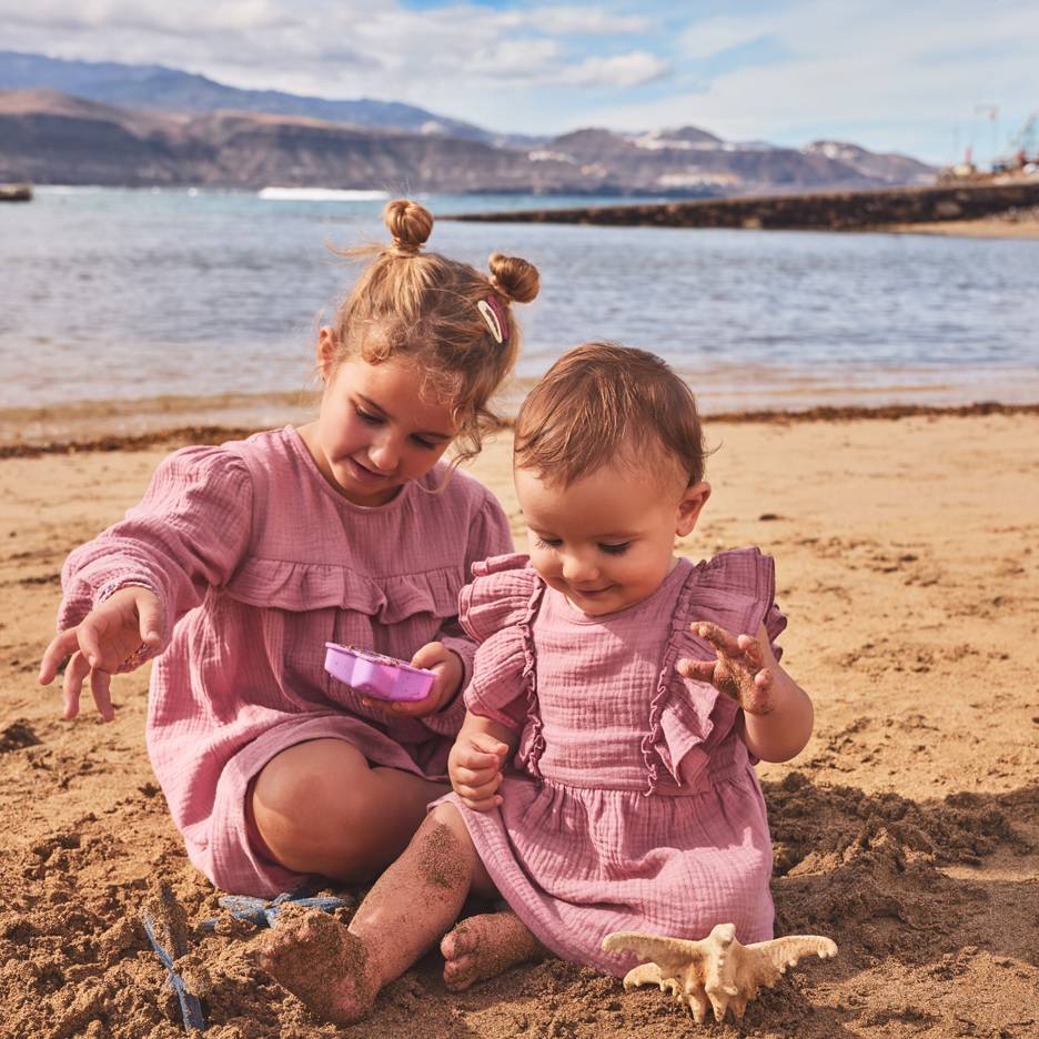 Dvije djevojčice u ružičastim haljinama igraju se u pijesku na plaži.