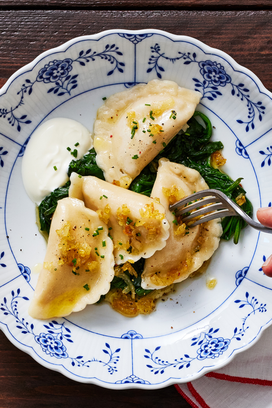 Tanjur s pierogima, špinatom, kiselim vrhnjem i prženim lukom.