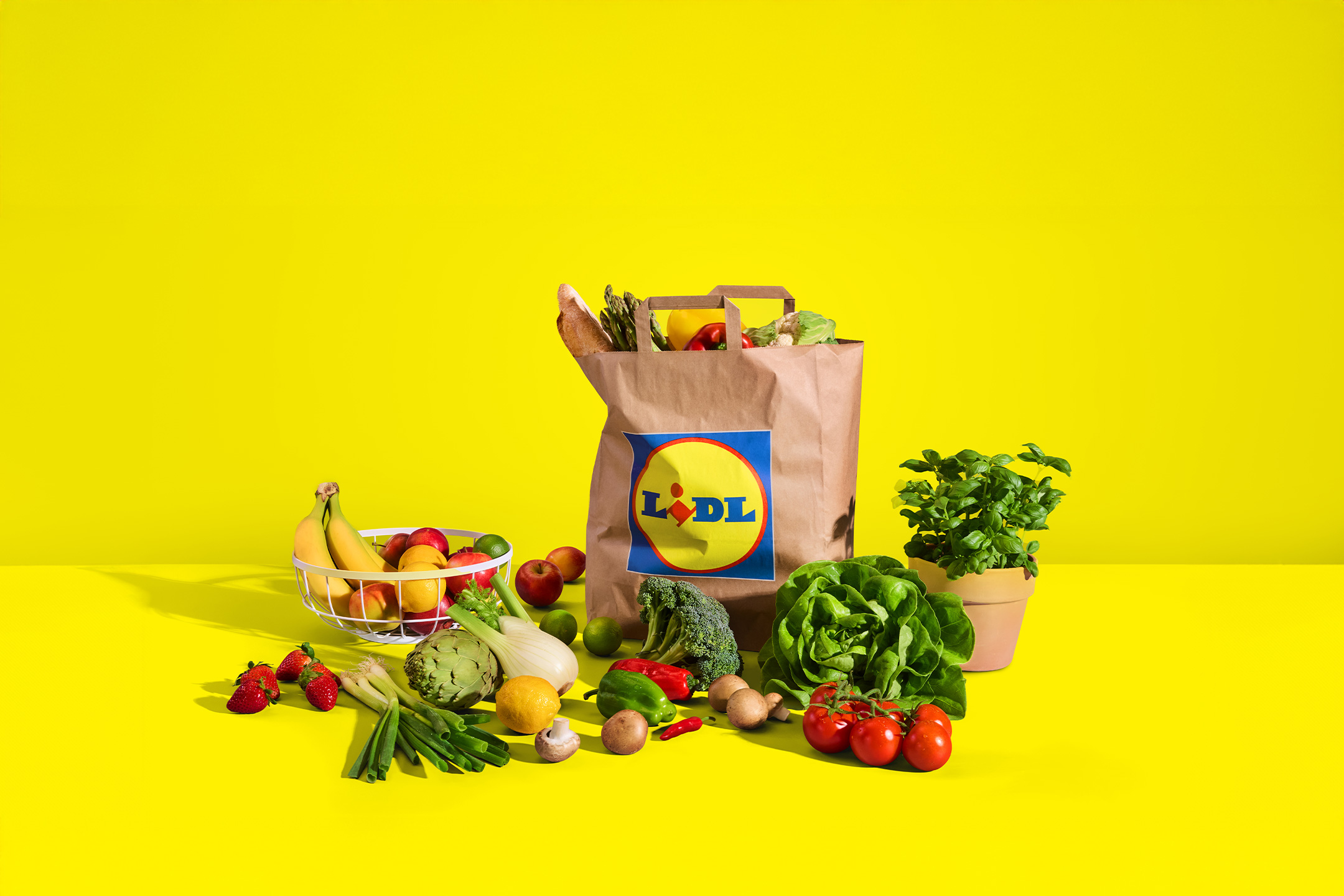 Lidl papirnata vrećica s namirnicama, voćem i povrćem na žutoj pozadini.