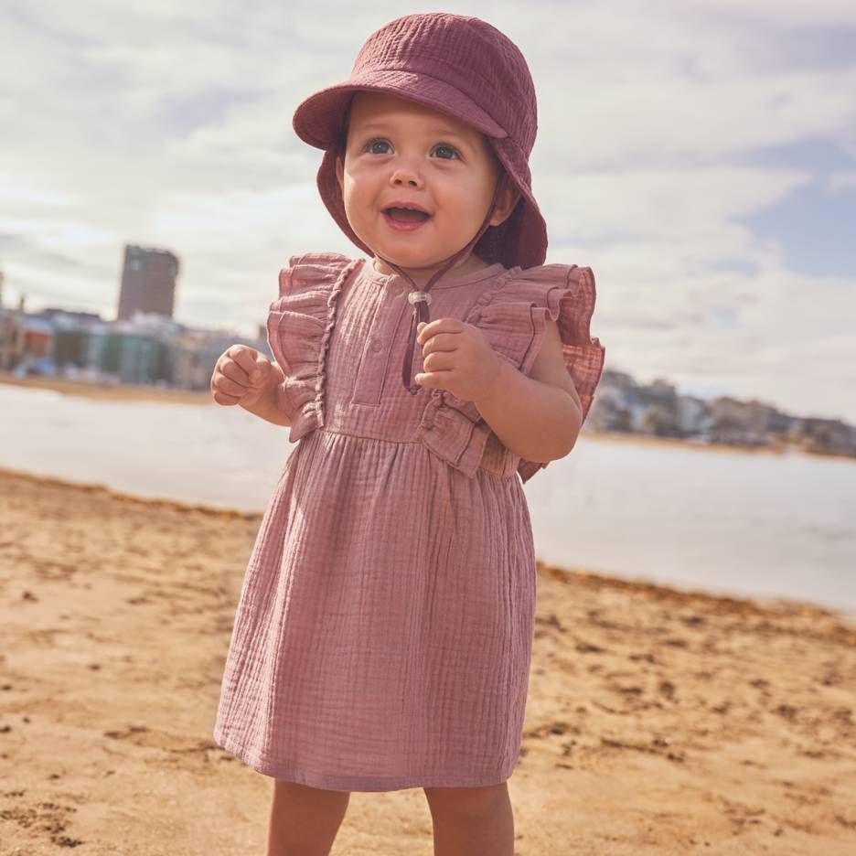 Beba u ružičastoj haljini i šeširu na plaži.